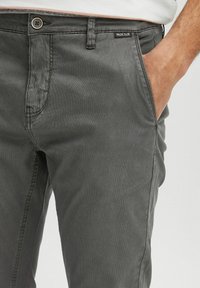 Pantaloni grigi in cotone con vestibilità slim, dotati di tasche frontali, un bottone visibile e un'etichetta con logo orizzontale sulla vita.