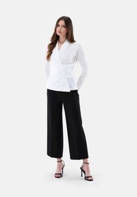 Top bianco con maniche lunghe, tessuto testurizzato e vita a peplum abbinato a pantaloni neri a gamba larga. Tacchi neri con fasce accentuano l'outfit.