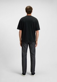 Black short-sleeve t-shirt with a round neckline, worn with dark grey jeans and black sneakers, viewed from the back. Smooth fabric, casual fit.
