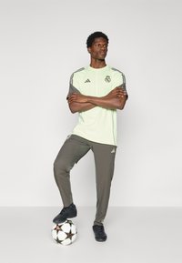 Light green athletic shirt with gray sleeves and logo, paired with gray track pants. Black soccer shoes and ball included.