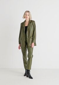 Olijfgroene faux leren blazer en broekset, met een gestructureerd ontwerp, twee voorzakken en elegante zwarte haklaarzen.