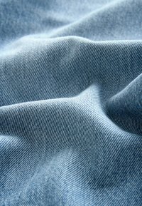 Gaiši zils džinsa audums ar gludu tekstūru, kas raksturojas ar klasisku divvirzienu auduma rakstu un smalkām krāsu variācijām.