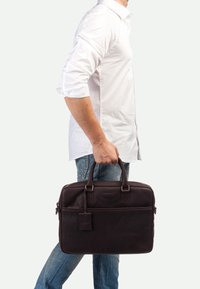 Braune Lederaktentasche mit doppelten Griffen, vorderer Reißverschlusstasche und abnehmbarem Anhänger. Glatte Textur, rechteckige Form und robustes Design.