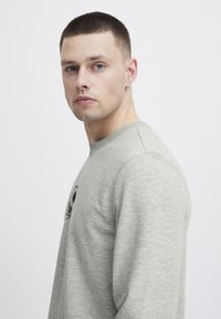 Lys grå sweatshirt med rund hals, ribbestrikkede mansjetter og et grafisk trykk på forsiden. Myk tekstur med en avslappet passform.