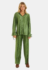 Conjunto de pijama de satén verde con un patrón texturizado y acanalado. La parte superior cuenta con un cuello de solapa y cierre de botones, mientras que los pantalones tienen aberturas laterales.