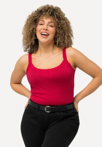 Rotes, ärmelloses Tanktop mit Rundhalsausschnitt und breiten Trägern; weiches, dehnbares Material. Kombiniert mit hochgeschnittenen schwarzen Jeans und einem Gürtel.