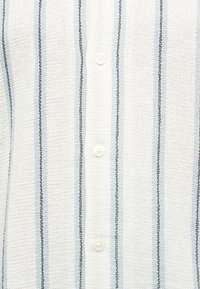 Λευκό υφασμάτινο υλικό με υφή, με κάθετες μαύρες και ανοιχτό μπλε ρίγες και τρία λευκά κουμπιά στο κέντρο ενός πουκάμισου ή μπλούζας.