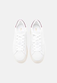 Paire de baskets blanches avec des lacets blancs et des accents violets au talon, vues de dessus sur un fond gris clair.