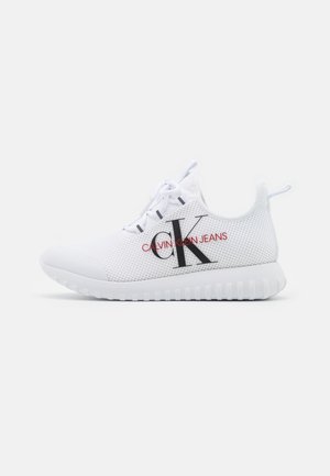 Witte atletische schoen van mesh met witte zool en veters, voorzien van een groot zwart "CK"-logo en rode tekst "Calvin Klein Jeans" aan de zijkant.