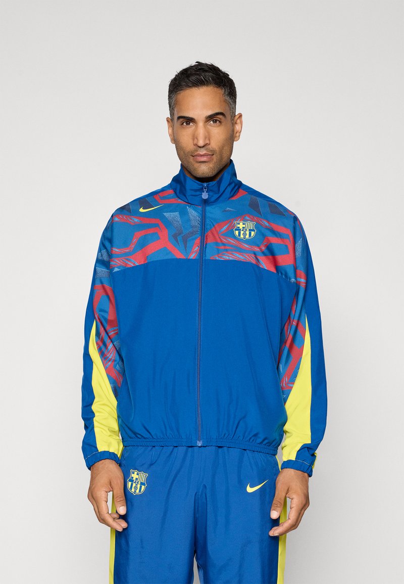 Modrá sportovní bunda s červenými a žlutými akcenty, s vysokým límcem, zipovým zapínáním a logem na hrudi. Vyrobena z lehkého, hladkého materiálu.