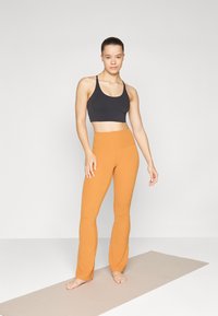 Sportovní podprsenka v černé barvě a vysoké legíny v oranžové barvě; obojí vyrobené z pružného materiálu, upevněný design, hladká textura, bez vzorů.