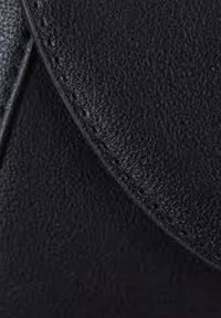 Pelle nera texturizzata con bordo liscio e curvo e cuciture visibili; una vista ravvicinata che mette in evidenza la finitura e i dettagli del materiale.