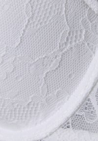 Soutien-gorge en dentelle blanche avec un motif floral texturé et des bords lisses. Il présente une doublure en microfibre douce et des bretelles fines et ajustables.