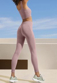 Sujetador deportivo de color rosa claro combinado con leggings de cintura alta a juego, con un diseño texturizado. Complementado con zapatillas deportivas verdes.