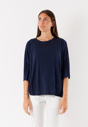 T-shirt oversize blu navy, morbido e leggero, con scollatura rotonda e maniche corte. Indossato con pantaloni bianchi.