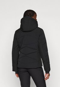 Melna pildīta jakas ar kapuci. Tajā ir kvadrātu dizains, nedaudz teksturēta auduma, kā arī garas piedurknes ar ribotām aprocēm.