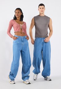 Top cropped de manga longa em padrão de gingham vermelho e branco com decote amarrado, combinado com jeans oversized de denim azul claro e sapatilhas. Top sem mangas cinza.