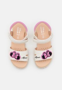 Vita sandaler med rosa accenter, som har en Minnie Mouse-design på remmen och perforerad sula, märkt "GEOX" och storlek "27."