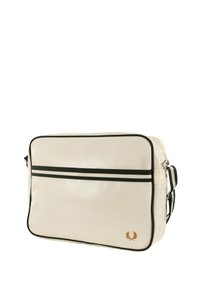 Borsa sintetica beige con strisce e rifiniture verde, caratterizzata da un emblema dorato. Forma rettangolare con tracolla regolabile e chiusura con zip.