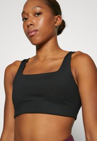 Black cropped sports bra with wide straps, square neckline, smooth texture, and minimal seams. Suitable for active wear.