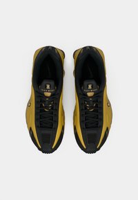 Ζευγάρι χρυσών και μαύρων Nike Shox παπουτσιών που φαίνονται από πάνω, δείχνοντας τα κορδόνια, τα λογότυπα και το μαξιλαράκι στο εσωτερικό.