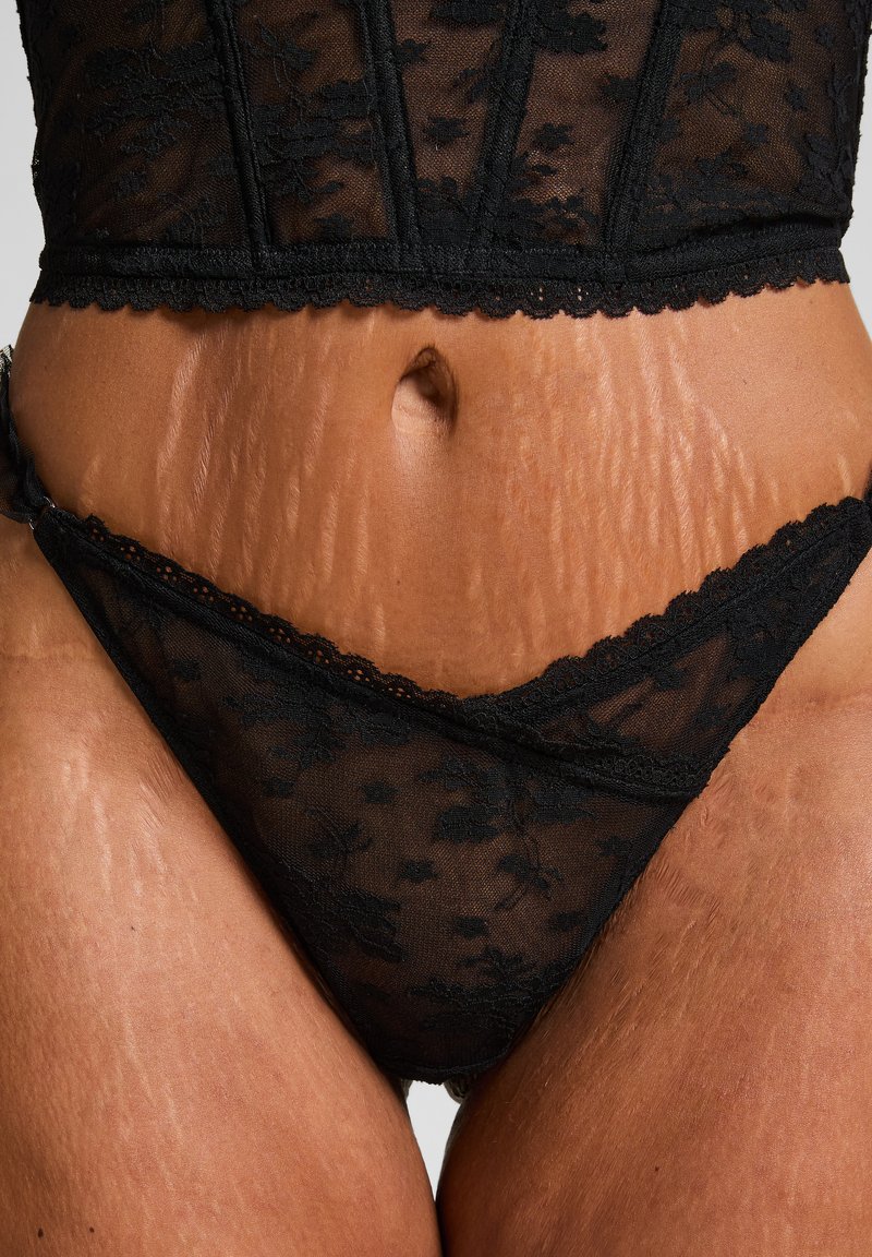 Zwart kanten lingerieset met complexe bloemmotieven, doorzichtige textuur, gegolfde randen en een laag gesneden stringontwerp.