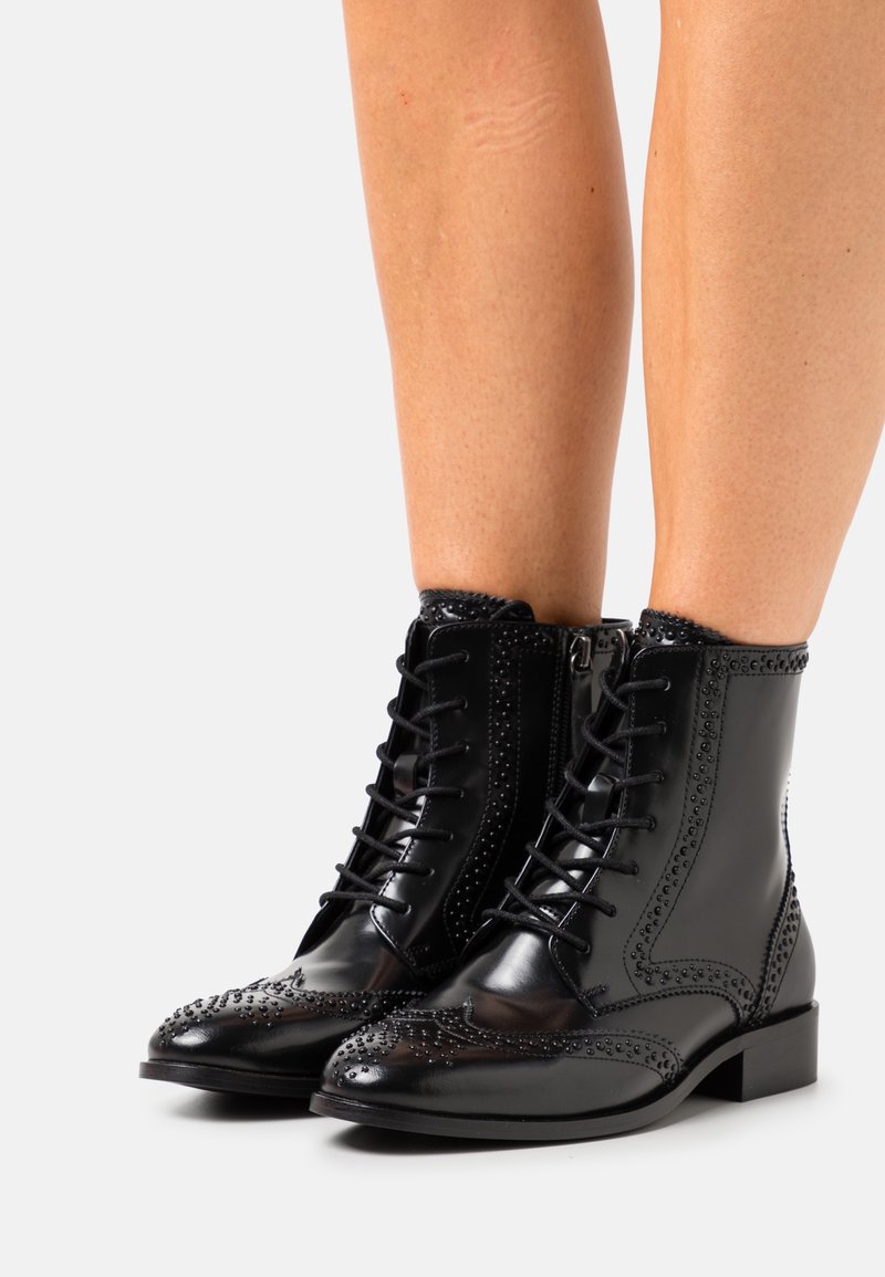 Bottines en cuir noir avec un design à lacets, des détails brogue et des clous décoratifs le long des bords. Bout carré et talon modeste.