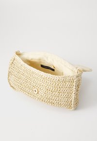 Bolso de mano trenzado en color beige con cierre de botón magnético y forro interior de tela, abierto para mostrar un pequeño bolsillo interior.