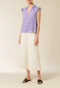 Blusa lavanda con maniche a volant, tessuto testurizzato e motivi a cuore blu, abbinata a pantaloni bianchi a gamba larga e sandali neri.