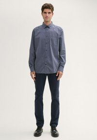 Dunkelblaues Button-Up-Hemd für Herren, mit langen Ärmeln, Brusttasche, aus strukturiertem Stoff, kombiniert mit dunklen Hosen und schwarzen Schuhen.