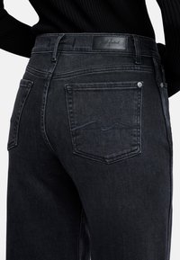 Jeans in denim scuro con una texture liscia, dotati di tasche posteriori e di un'etichetta in pelle sulla vita. Dettagli di cucitura sottili sulle tasche.