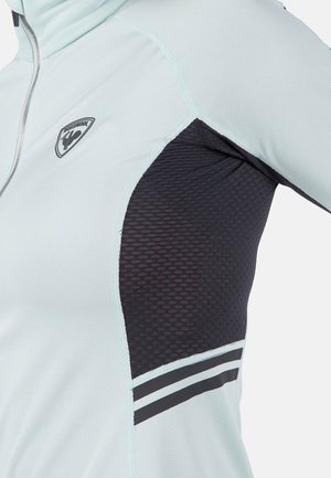 Błękitna kurtka sportowa z czarnym siateczkowym panelem, srebrnym zamkiem błyskawicznym, logo na klatce piersiowej oraz paskowanymi akcentami na rękawie. Teksturowana tkanina.