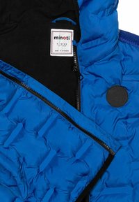 Giacca blu imbottita con interno nero, chiusura a zip e patch con logo. Presenta una texture trapuntata e una fodera in tessuto morbido.