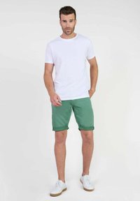 Witte ronde hals t-shirt, groene shorts met gerolde zoom en witte sneakers metbruine zolen. Minimalistisch ontwerp zonder patronen of accenten.
