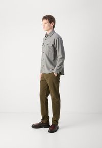 Chemise en flanelle grise avec deux poches poitrine, fermeture à boutons et poignets ; associée à un pantalon en velours côtelé vert olive ; chaussures noires et bordeaux.