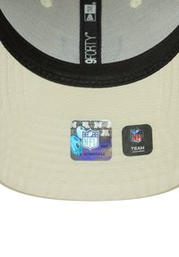 Visera de gorra beige con etiqueta holográfica de la NFL y etiqueta negra de Team Headwear debajo del forro interior negro y etiqueta "9FORTY".