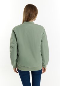 Groene bomberjack met een gladde textuur, geribde manchetten en zoom, en een klassieke kraag, gecombineerd met strakke blauwe jeans.