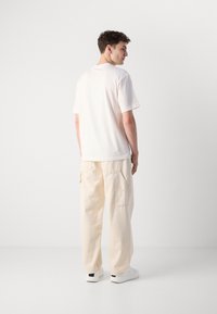 Bomuld T-shirt i cremefarve med korte ærmer, parret med lysebeige cargo bukser med sidelommer og en løs pasform.
