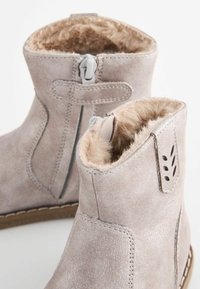 Stivaletti alla caviglia grigio chiaro con una finitura in suede testurizzato e imbottitura in pelliccia artificiale. Chiusura con zip laterale e dettagli in cucitura decorativa sulla parte esterna.