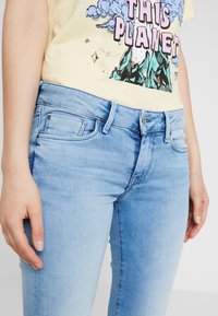 Svetle modré denimové džíny s přiléhavým střihem, vybavené předními kapsami, knoflíkovým zapínáním a jemným vyblednutím pro strukturovaný vzhled.