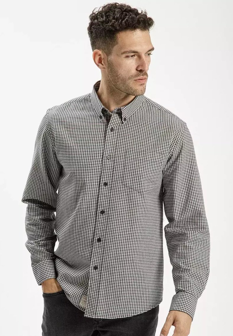 Czarna i biała koszula z długim rękawem w kratę, z klasycznym kołnierzykiem i jedną kieszenią na piersi. Z tkaniny bawełnianej o delikatnej fakturze.