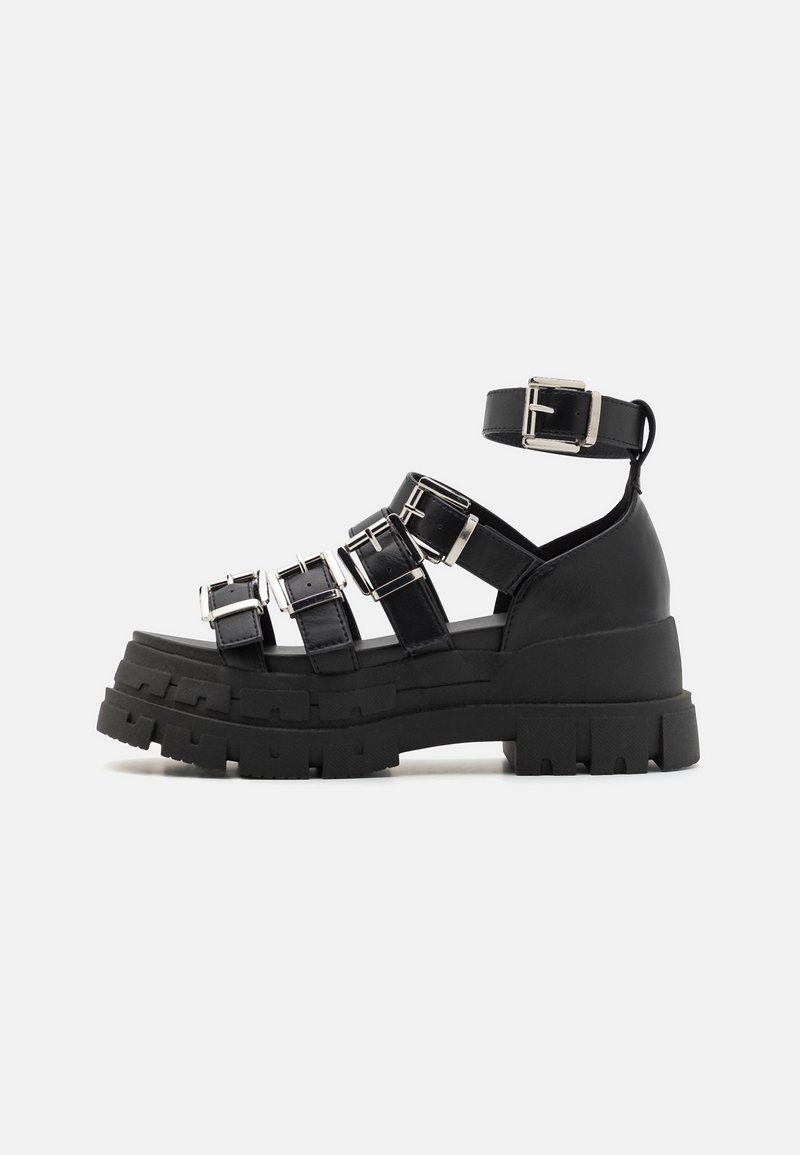 Sandales à plateforme noires avec plusieurs sangles à boucle, un large lit de pied et une semelle en caoutchouc texturée pour une meilleure adhérence et stabilité.