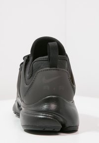 Černá sportovní bota s hladkým koženým svrškem, polstrovaným límcem a poutkem. Obsahuje strukturovanou podrážku a diskrétní branding na patě.