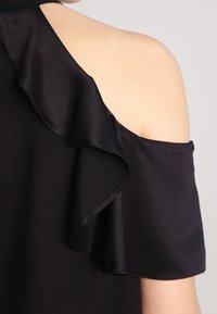 Abito nero con spalle scoperte e un sovrapposto di satin arricciato, texture elegante. Il design a spalla scoperta mette in risalto la pelle liscia sottostante.