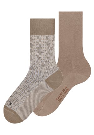 Een paar beige jurk sokken, een met een geometrisch wit patroon, de ander effen beige met "FALKE SENSITIVE LONDON" gedrukt op de zool.