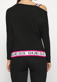 Maglione nero con scollo ampio, caratterizzato da un design off-shoulder e da un elastico con logo rosa e bianco lungo l'orlo.