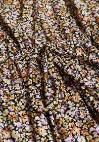 Tejido con estampado floral que presenta flores naranjas, rosas y amarillas sobre un fondo negro; textura suave con detalles fruncidos y lazos.