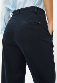 Pantalons bleu nuit en tissu lisse, à taille haute, avec des poches latérales et une poche arrière avec une finition soignée.