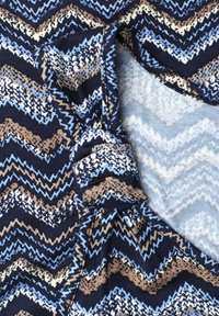Gros plan d’un tissu plié avec des motifs zigzag en bleu, beige, blanc et noir, montrant la texture et les détails du tricot.