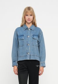Denim jakk, helesinine, nööpidega ees, kaks rinda taskut, lühendatud disain, nähtavad õmblustead, kombineeritud mustade pükstega.